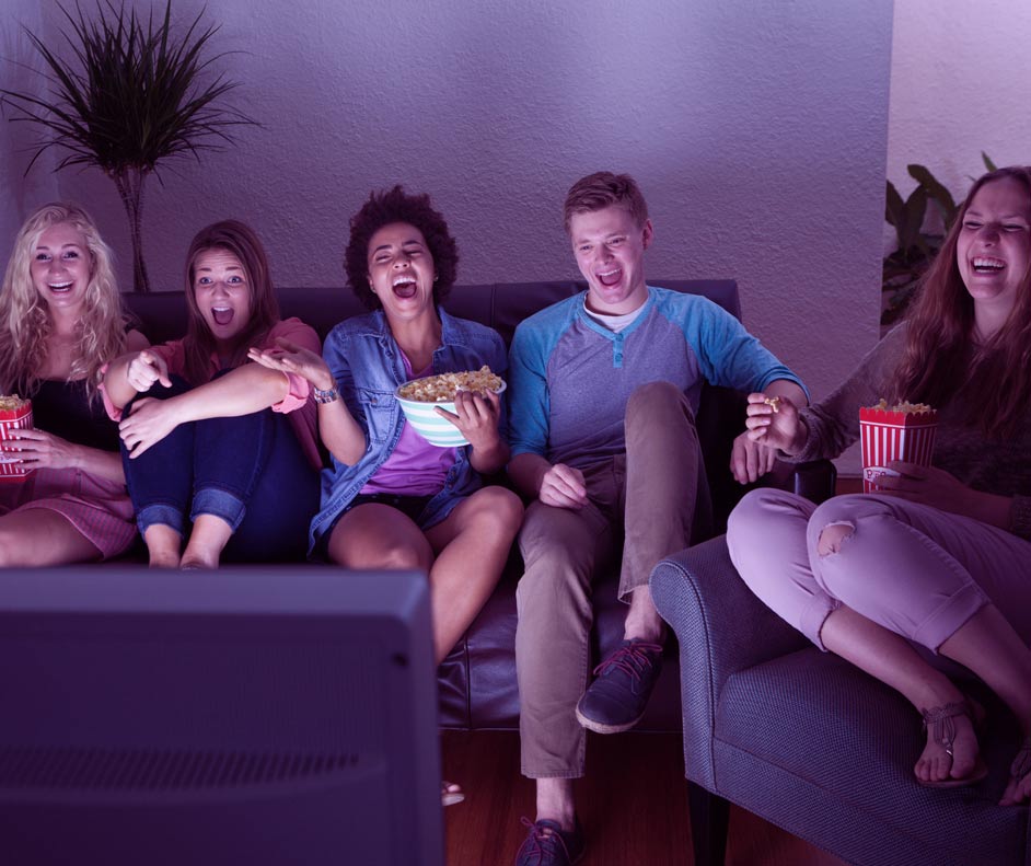 Imagem de um grupo diverso de amigos sentados no sofá da sala assistindo televisão.