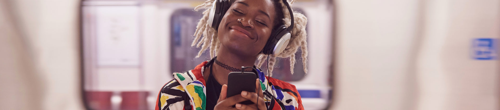 Imagem de uma moça sorrindo e ouvindo música com fones de ouvido.