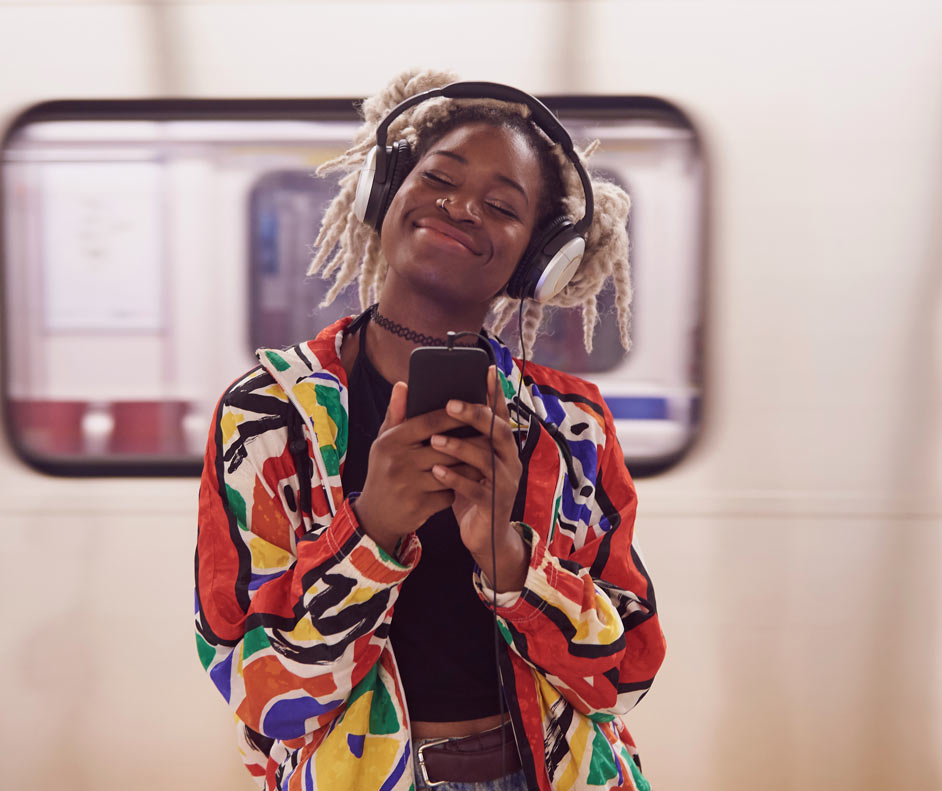 Imagem de uma moça sorrindo e ouvindo música com fones de ouvido.