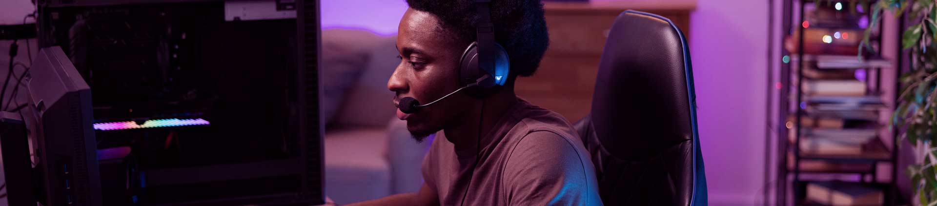 Homem negro sentado na cadeira mexendo no computador. Parece utilizar um tipo de teclado gamer