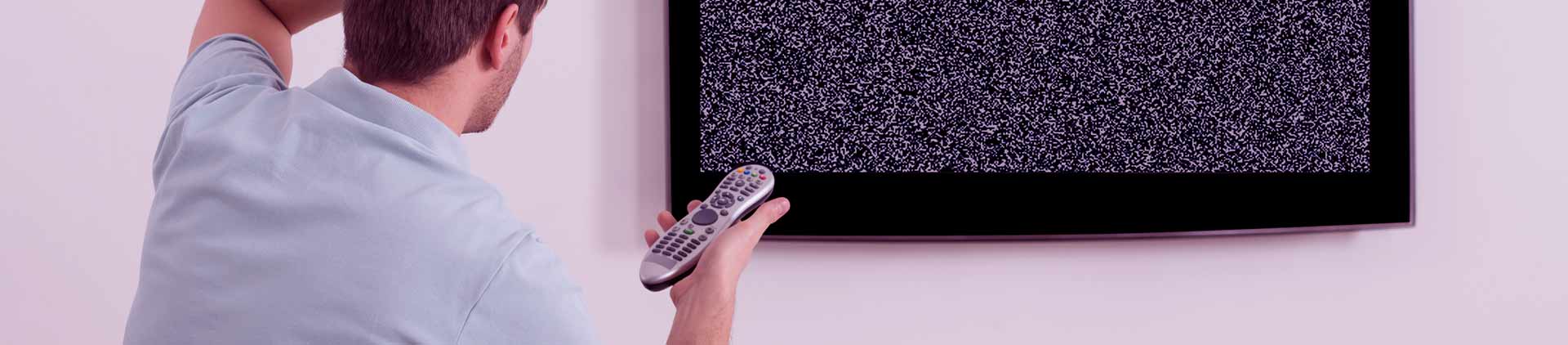 Homem coçando a cabeça enquanto segura o controle em direção a TV. O aparelho parece sem sinal