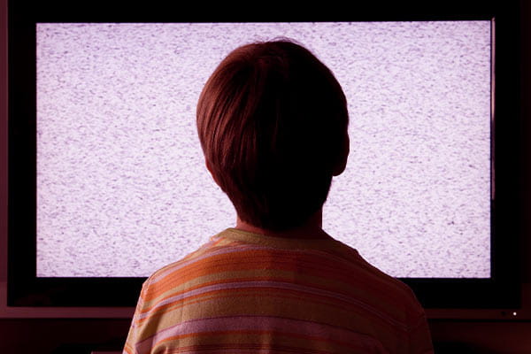 Menino sentado em frente à TV sem sinal com chiado