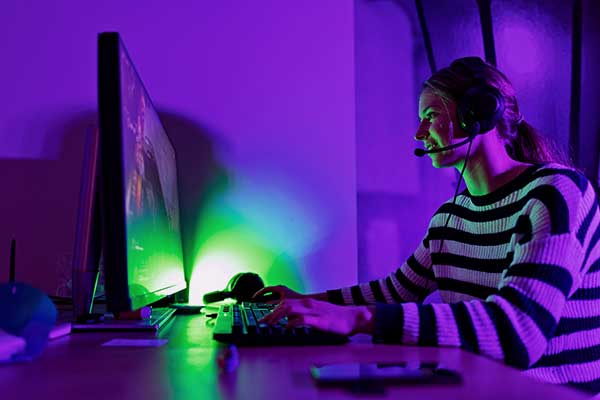 Moça com headphone jogando num PC com upgrade sentada em uma mesa gamer