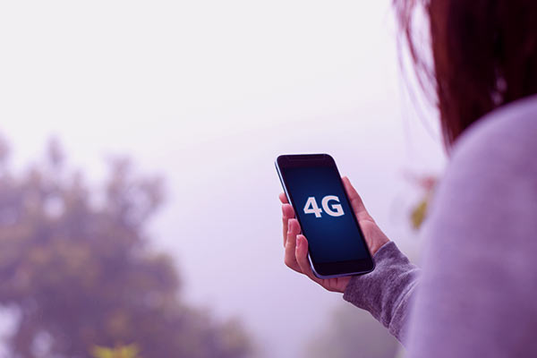 Mulher segurando um celular com uma mão e na tela aparece escrito 4G