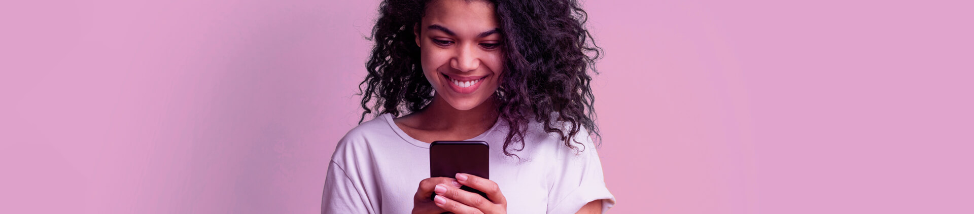 Imagem de uma mulher sorrindo enquanto usa um celular em frente a um fundo rosa