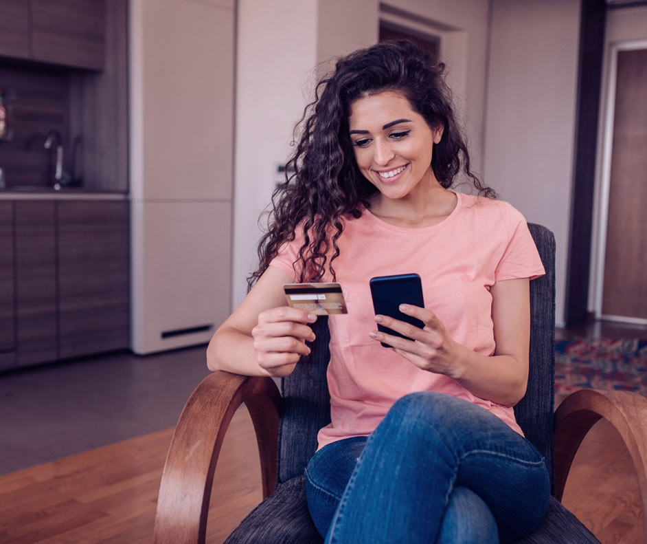 Imagem de uma mulher sorrindo segurando um cartão de crédito e um celular.