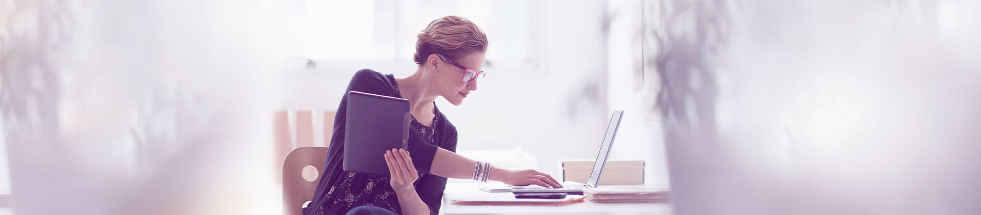 Imagem de uma mulher configurando seu notebook enquanto segura um tablet.