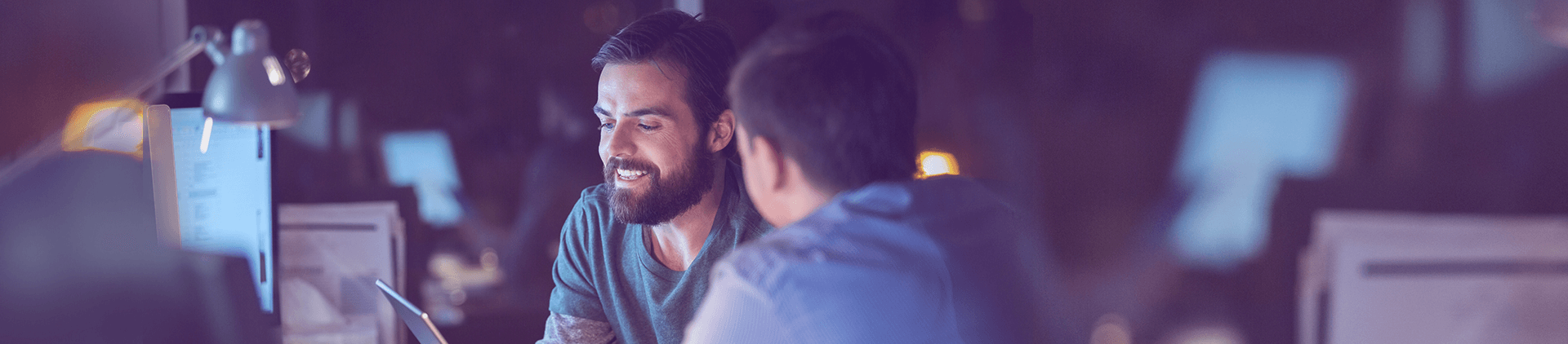 Foto com dois homens conversando em uma ambiente de trabalho. Um deles segura um tablet.